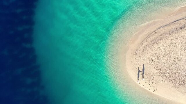 cute couple walks hand in hand on the beach with long shadows in the sun, circling Zlatni Rat beach with crystal clear turquoise sea