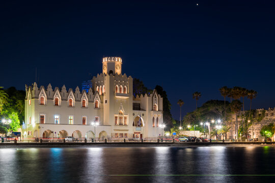 Night view of the municipal building with The caste of the Knights and palm trees in Kos town, Kos island, Greece