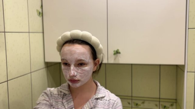 young teeneger girl making white facial mask in her own green bathroom. skincare, face cream morning evening rotine