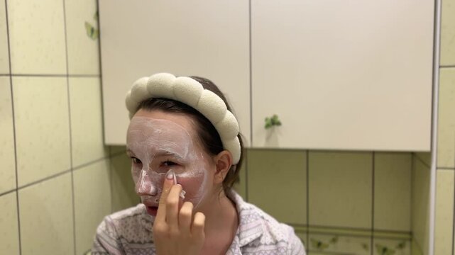 young teeneger girl making white facial mask in her own green bathroom. skincare, face cream morning evening rotine