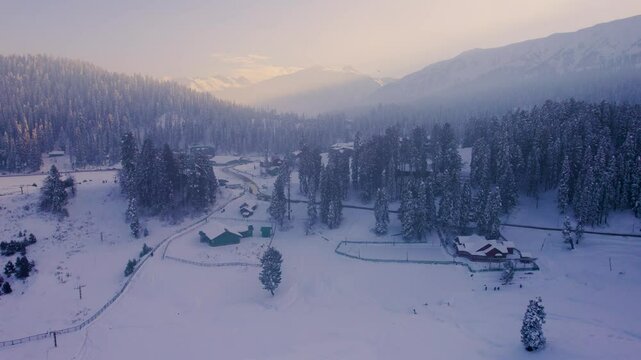 Aerial drone shot flying forward towards snow covered houses surrounded by forest of chinar walnut trees and the Himalaya mountains as the backdrop in Paradise on earth Kashmir