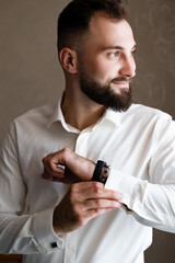 A portrait of a man in a white dress shirt, meticulously adjusting his cufflinks and wristwatch. He...