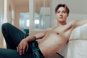 Fit and Handsome: Shirtless Man Takes a Post-Workout Break, Leaning on Sofa and Gazing at Camera After a Sweaty Day in the Office