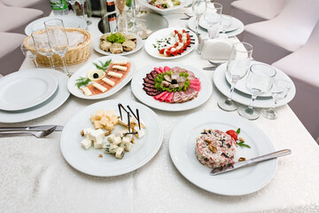 A meticulously arranged buffet table displays an array of delicious appetizers, including cheese, cured meats, and other delicacies.  White plates and silverware add to the elegant setting.