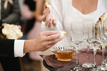 Close-up of hands sharing bread dipped in honey.  Empty glasses and additional bread are visible, suggesting a shared meal or ceremony. The atmosphere is warm and intimate.