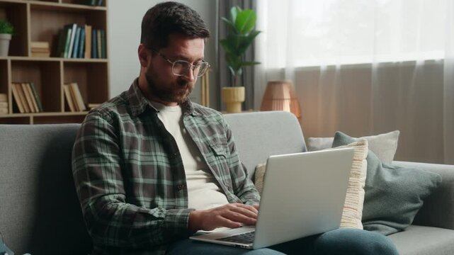 Adult freelancer businessman business man at home guy male author user using laptop typing writing article at computer internet online working at home couch thinking ponder web net job shopping decide