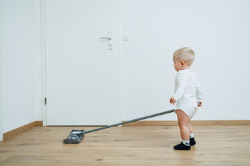 Little boy washes the floor with a mop. Toddler cleans at home. Mop for cleaning in the apartment.