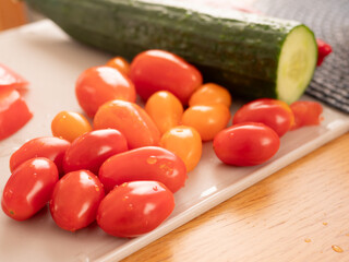 Fresh cherry tomatoes and cucumber preparing for salad on cutting board