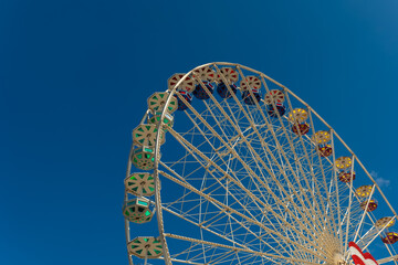 Bright ferris wheel stands against a clear blue sky at a summer fairground attracting fun seekers...