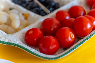 Fresh red tomatoes arranged on a decorative plate next to assorted fruits in a vibrant kitchen setting