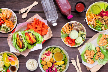 Healthy take out fast food table scene. Overhead view over a dark wood background. Lettuce bean burgers with sweet potato fries, nutritious bowls, lettuce wraps and smoothie drink.
