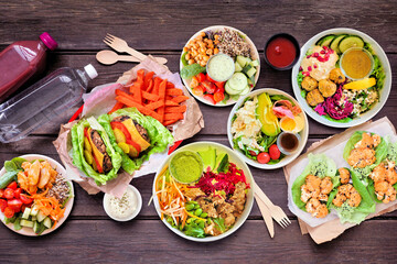 Healthy take out fast food table scene. Above view over a dark wood background. Lettuce bean burgers with sweet potato fries, nutritious bowls, lettuce wraps and smoothie drink.