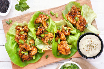 Healthy lettuce wraps with honey garlic grilled cauliflower. Top down view table scene over a white wood background. Plant-based diet concept.