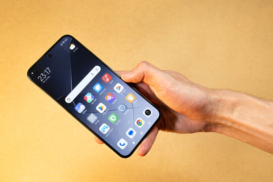 Man's hand holding a new modern Xiaomi android smartphone with main home screen display, default apps visible, new mobile phone buying concept, simple background, close-up