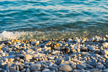 Smooth, multicolored pebbles of the beach in Nice, France, washed by turquoise waves: the perfect backdrop for summer holidays and relaxation in nature.