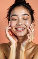 Young Asian woman with healthy skin. Portrait of beautiful girl with natural makeup. Touches face gently. Happy expression, glowing skin. Studio shot against peach background. Skincare, cosmetics