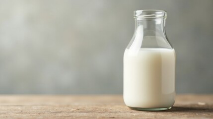 A glass bottle filled with creamy milk sits on a rustic wooden surface against a muted background.