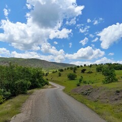 A photograph of a rural location in the Koyulhisar district of Sivas province, with green hills and trees covered with blue sky and clouds.