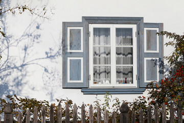 Wooden window with rustic shutters surrounded by a charming autumn garden. Traditional architectural facade natural wood and wooden fence in countryside scene.