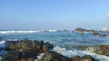 Scenic view of a rocky seashore with gentle ocean waves under a clear blue sky. Tranquil coastal landscape perfect for themes of nature, serenity, travel, and relaxation