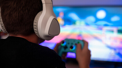 Boy playing video game at home while wearing headphones, focused on screen, enjoying digital...