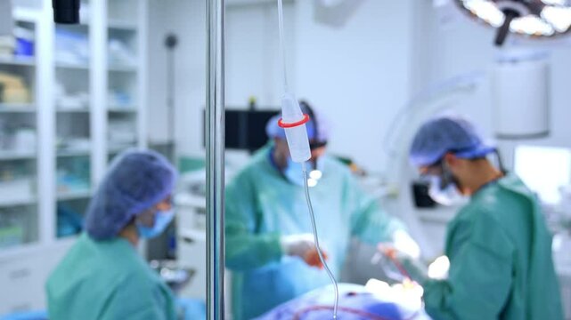 Drop counter on the stand in the surgery room. Medical team operating a patient at blurred backdrop.