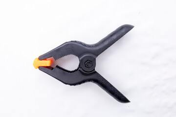 Black plastic spring clamp with orange tips lying on white marble background