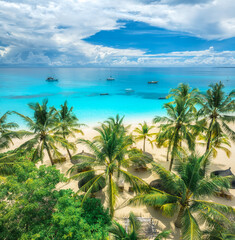 Fototapeta premium Aerial view of white sandy beach with palm trees, sunbeds, umbrellas, yachts, boats, blue ocean, sky with clouds at sunset. Summer in Kendwa, Zanzibar island. Tropical landscape. Clear sea. Top view