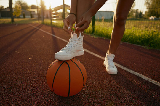Female basketball player tying shoelaces putting foot on ball - Powered by Adobe