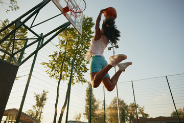 Young woman basketball player frozen in motion jumping high making slam dunk