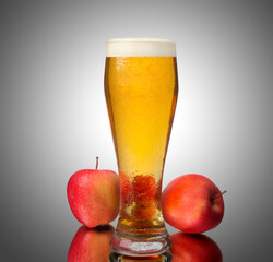A glass of beer is next to two apples