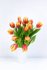 Bouquet of fresh natural red-yellow tulips in a white vase. Greeting card.
