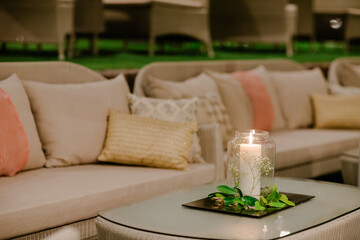 Relaxing outdoor seating area with a lit candle and decorative greenery. Soft lighting and neutral tones create a serene ambiance.
