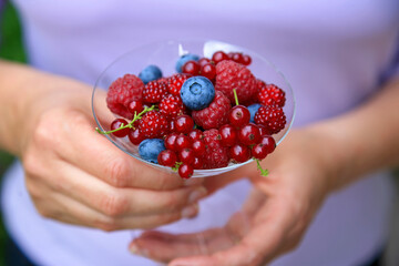 Hand holding a champagne glass filled with Raspberries, Japanese wineberries (Rubus phoenicolasius) and blueberries