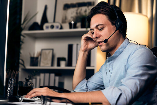 Call center consulting with customers on headphones on monitor in business paragraph with typing on pc with dynamic data marketing analysis planning at modern home office at night time. Pecuniary.