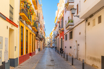 Fototapeta premium A narrow street of traditional whitewashed and brightly painted buildings in the downtown district of the Andalusian city of Seville, Spain.
