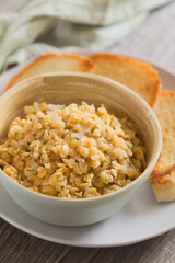 Fresh homemade vegan spread or salad made with split red lentil, onion, garlic and parsley, served in bowl with toasted bread on plate (Selective Focus, Focus on the front of the lentils)