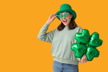 Beautiful young woman in leprechaun hat and decorative glasses with air balloon in shape of clover...