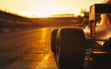  The rear wheel of a Formula 1 car on a racetrack at sunset. The sunlight reflects off the track and the car, creating a warm, golden glow.image © Michael