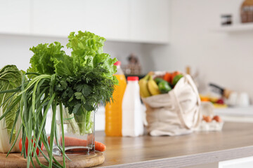 Bag full of fruits and vegetables near glass with greens in kitchen