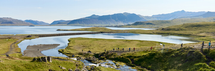 Tourists hiking along waterfall stream in Iceland. Group following trail by rushing water with...