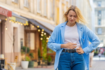 Sick ill young blonde woman suffering from period cramps painful stomach ache outdoors. Lady girl...