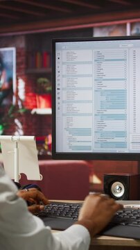 Vertical video Programmer at computer desk coding, creating software, implementing algorithms. African american IT specialist in home office working with code editor, building applications, camera A