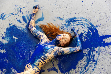 sexy upper part of a redheaded woman in blue color painted on the floor, abstract body art painting.