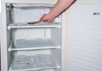 ice has formed on the walls of the freezer and it is creeping out, a woman's hand is knocking the ice off with a wooden spatula,
