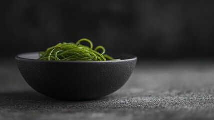 Close-up of green pasta in a dark bowl on a gray surface.
