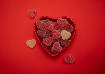 Heart-shaped gummy candies in a heart-shaped bowl on a vibrant red background, symbolizing love and romance. Ideal for Valentine's Day, weddings, anniversaries, and romantic celebrations.