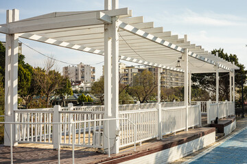 Modern white pergola in urban park with cityscape background