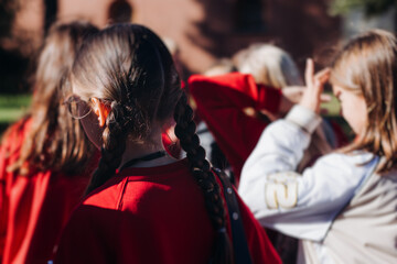 Obraz premium Group of school pupils and students on outdoor excursion tour in the city streets with guide, a docent with a tourist young visitors wearing red, school field trip, urban tour in the summer sunny day