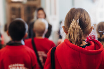 Group of kids children on excursion in a museum gallery, school pupils and students tour with guide, a docent with a tourists, young visitors wearing red, school field trip, art exhibition attendees